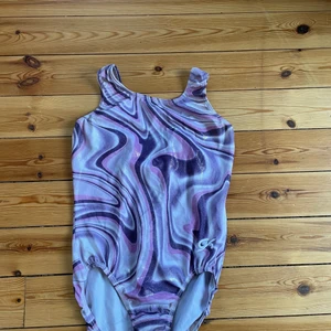 Gymnastikdräkt - Gymnastikdräkt i bra skick med fint marmorerat mönster. Glansigt spandex tyg, håller bra. Inga fläckar eller lösa sömmar. Skickas tvättad. Originalpris 400 kr. 