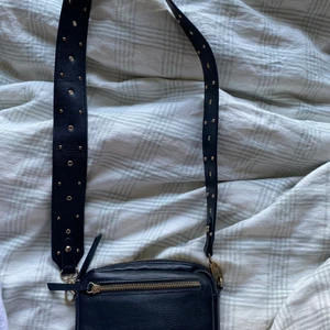 Svart väska med nitar - Säljer nu min fina svarta axelremsväska! Köpte den för några år sedan, doxk varsamt använd samt oanvänd det senaste året. Väskan har gulddetaljer och ett stort fack, man får plats med mycket!! Axelremmen har guldfärgade nitar. Inköpt för 500kr, pris går att diskuteras❣️❣️❣️💌💌