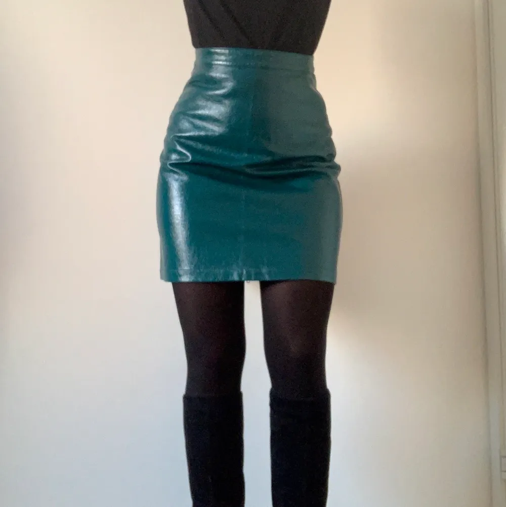 Faux leather A-line skirt in a beautiful petrol green colour (on the pictures the skirt appears more blue than in real life). There is a zipper in the back. The skirt is highwaisted and fits to mid-thighs. It is fitted on me, but can also be less fitted on someone of a smaller size than me. The skirt has never been worn before so it is in perfect condition. . Kjolar.
