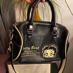 Skit snygg väska med tryck av den legendariska Betty Boop figuren. Väskan är i mycket bra skick och har ett avtagbart axelband. Köpt här från Plick och säljer då den inte kommer till så mycket användning😢