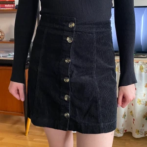 Kjol i manchester - Svart kjol i manchester med knappar framtill. Storlek 36. Knapparna går att knäppa upp hela vägen.