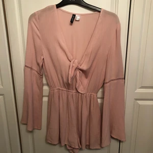 Byxdress från HM - Super fin somrig byxdress i ljusrosa med fina detaljer på ärmarna. Strl 32 men på mig passar den nästan så den passar på 34/36 människor också.   Hade denna på skolavslutningen i 6an och efter det aldrig mera använd tyvärr.   Knyts framtill   Då den är ganska djup urringning i (iaf för att användas på en skolavslutning för 6:e klassare) så är en knapp ditsydd men denna kan enkelt tas bort med en nagelsax eller liknande.   Lite fluffigare ärmar med en superfin detalj på strax ovanför armvecket.   Undrar du något kolla profilen eller kika in i chatten