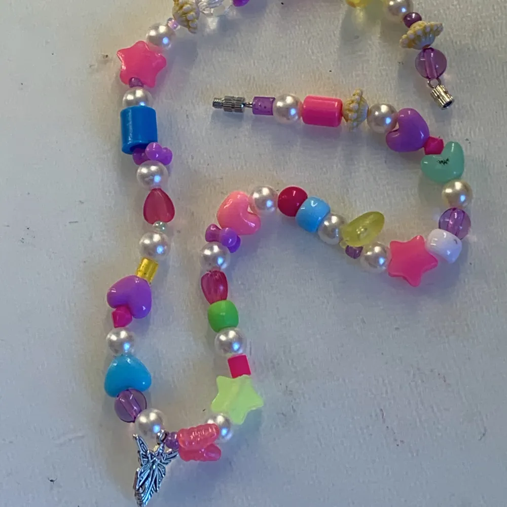 Halsband med pärlor i olika färger, en silvrig älv-berlock och ett silverspänne☀️🧚💖. Accessoarer.