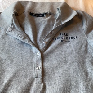 Peak performance t-shirt - En grå tröja med knappar och krage. Funkar för att ha på sig för alla. Fint material och tyg. Storleken är M men funkar för S också. frakt ingår. Tvättar såklart innan frakt.