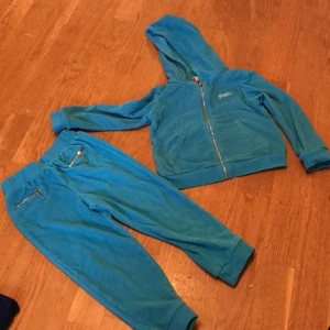 Juicy Couture turkost set  - Turkost Juicy Couture set med byxor med 2 fickor fram och jacka med stort tryck bak och ett mindre tryck fram. Materialet är frotté liknande. Jackan och byxorna kan vara lite slitna på vissa ställen men setet är helt väldigt fint. 