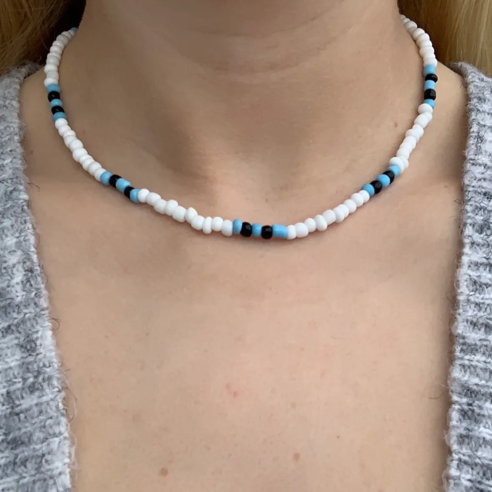 Vitt pärlhalsband med svarta och ljusblåa pärlor💙🤍🖤🦋 halsbandet försluts med lås och tråden är elastisk . Accessoarer.