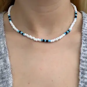 Vitt pärlhalsband med svarta och ljusblåa pärlor💙🤍🖤🦋 halsbandet försluts med lås och tråden är elastisk 