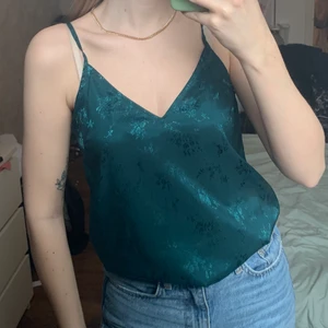 Grönt linne i sidenmaterial - Säljer detta mörkgröna linne i sidenmaterial med blommönster. Storlek 34 från H&M. Endast använd 2 ggr, nyskick.