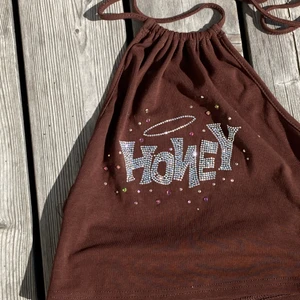 Jättecool topp🤎 - Säljer denna skitsnygga toppen med honeytryck av typ silvriga paljetter! 🤩 som man ser på bilden så är tröjan öppen i ryggen och knyts vid nacken! 💐 den är så fin men passar inte mig så säljer nu vidare! Säljer för 59 kr, om många är intresserade så blir det budgivningen lycka till!! 💞💞 