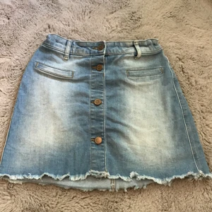 Kort jeanskjol - En blå, kort jeanskjol men 4 knappar, varav 2 av dom går att använda. Kjolen har använts ett fåtal gånger och är i väldigt bra skick. 