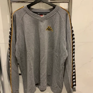 Kappa sweatshirt - Oversized grå sweatshirt från Kappa med orange, svart och vita detaljer på sidan. Aldrig använt den själv men köpt på Humana i Göteborg. Storlek L men passar även andra storlekar beroende på hur man vill att den ska sitta. Pris kan disskuteras, 66kr frakt tillkommer:)