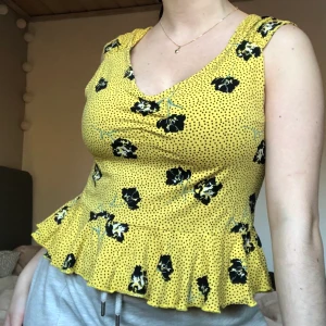 Gul tröja med volang s - Gul topp i skönt tyg med prickar på ch blommor på. Har volang nertill 