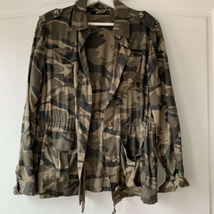 Snygg militärjacka  - En skitsnygg jacka i miltärmönster från Gina tricot i storlek 36. Den har knappar längs med och ett snöre i midjan så man får lite figur. Skitsnygg att ha en svart eller vit hoodie under eller en bandeautopp under på fest! Säljer pga att jag inte använder den längre då jag inte riktigt har den stilen💕💕