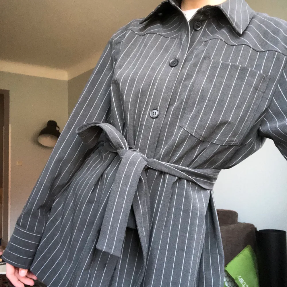 Snygg skjorta från weekday med en kostymkänsla! De tillkommer ett tyg skärp till som man kan knyta runt! Färgen är mörkgrå med vita stripes!. Kostymer.