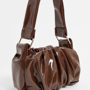 90-tals inspirerad väska - Jättefin brun väska i vinylliknande matrial. Säljer för att jag inte får användning för den. Det är ett stort rymligt fack och en inbyggd plånbok. 