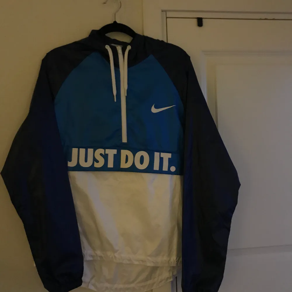 Blå och vit windbreaker från Nike med stor ficka på magen med öppning vid ”Just do it” texten. Beställde i för liten storlek så den är aldrig använd :). Övrigt.