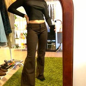 Bootcut lågmidjade bruna byxor - Bruna byxor med vita smala ränder. Superskönt material och de är i storlek 34 men jag har vanligast 36 och dom sitter bra på mig! 💘💘 midjemåttet är 80 cm ( de sitter mer på höften) och innerbenslängden är 79 cm!