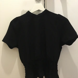 Gina topp - Svart topp, fint skick. Söta detaljer men piffigare ärmar, slits i nacken och ihop draget runt midjan!!