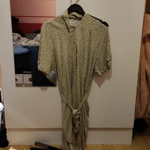 Blommig klänning med skärp - En längre klänning med blommigt mönster och bälte i snörformat. Mjukt och luftigt material