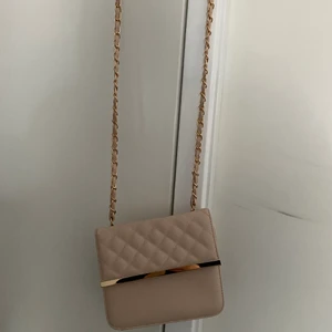 Ljusrosa axelväska med gulddetaljer - Säljer nu min ljusrosa axelväska med gulddetaljer pga att den inte används längre. Den är 16cm hög och 20cm bred.