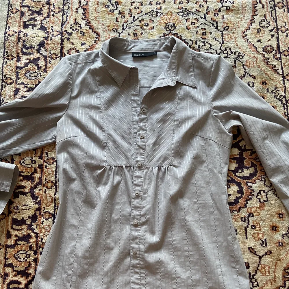 Figursydd grå/silver-randig skjorta med en väldigt smickrande passform!                                     Storlek 42                                            Material: polyester, bomull och elstan . Skjortor.