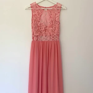 Oanvänd aftonklänning från NLY Eve/ stl: S/ långklänning  - Oanvänd aftonklänning från Nelly. Storlek S (36-38). Klänningen stängs i nacken med knapp och nedtill med dragkedja samt hake. Mycket fint skuren i ryggen. Normal i storlek och längd. 100 % polyester. Färg: pastellrosa/ aprikos. En extraknapp följer med.