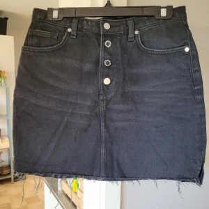 Jeanskjol - Mörkgrå jeanskjol med synliga knappar. Aldrig använd! Storlek 40. Från djur- och rökfritt hem. Kan skickas mot fraktkostnad.