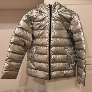 Silvergrå dunjacka, stl 160, Helt ny! - En Silvergrå dunjacka. Helt ny. Storlek 160, L60 B52.  OBS Den har en reva på baksidan som är 13 cm.