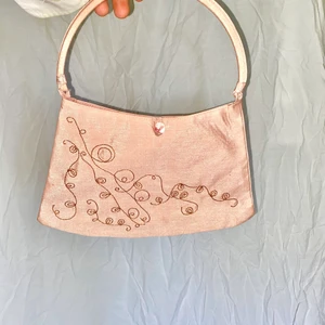 Rosa väska - Söt rosa liten väska broderad med glittertråd och pärla. Liten men relativt rymlig, fräsch och oanvänd. Från The Body Shop. Färgen stämmer lite halvbra överens med bilderna men den är ljusrosa skimmrig med kopparfärgad tråd. 