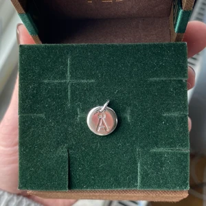 Brelock - En liten silvrig brelock från pilgrim med ett  Ä på som går att hända på en kedja från ett halsban eller armband☺️