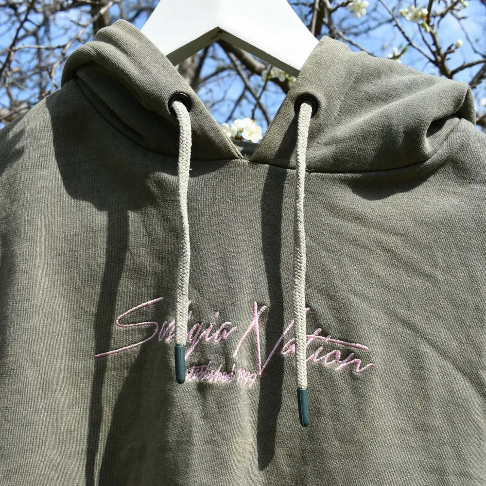 En grön hoodie med rosa text. Den är mycket använd och snörena är slitna. Men dom går att dra ur om man vill. Skriv om ni vill ha flera bilder😊. Hoodies.