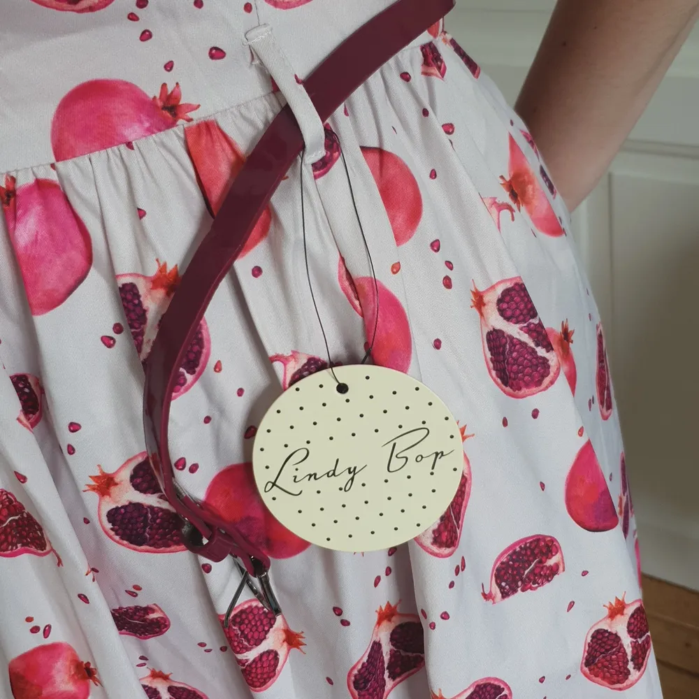 Vit Rockabillyklänning i nyskick med lila granatäpplemönster, krage och bälte. Klänningar.