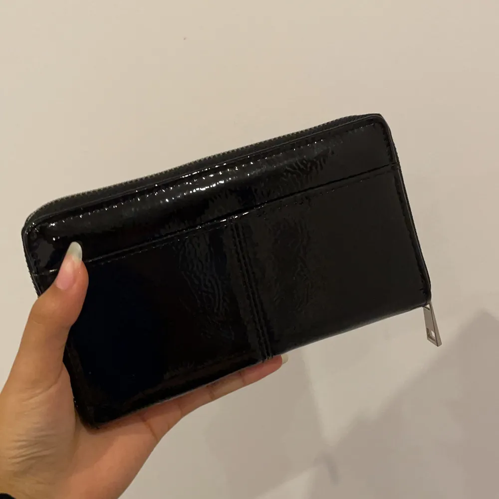Säljer denna snygga svarta plånbok från Lindex då den inte kommer till användning☺️ Är nästan inte använd alls, den har ett fack med dragkedja i mitten och kortfickor och fickor för kontanter inuti på sidorna. En ficka på framsidan. Jättefin detalj till din outfit🌸. Väskor.