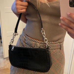 Svart väska  - Snygg svart väska med silverdetaljer från Glitter. Knappt använd, nyskick! Rymmer telefon osv.