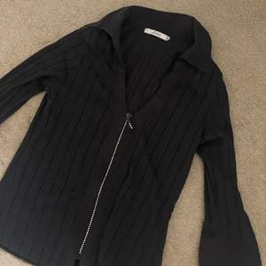 Svart blus med strass - Svart blus med dragkedja med strass. Superfin och bekväm. Mqn kan ha den knäppt eller uppknäppt beroende på vad man gillar. Skriv för bilder hur den sitter på!!