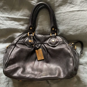 Marc by Marc Jacobs groove bag - Svart Marc by Marc Jacobs groove bag i den större modellen. Sjukt snygg och använde mycket förut men nu har jag en annan så denna får inte så mycket användning längre. Jag har även med det längre axelbandet så man kan antingen ha den på axeln eller bara låta den hänga som en fin detalj. Dessa säljs inte längre men nypris ligger på ca 4000kr! Hör av er om ni har bud eller frågor! (Den har några blåa fläckar ifrån en penna invändigt)