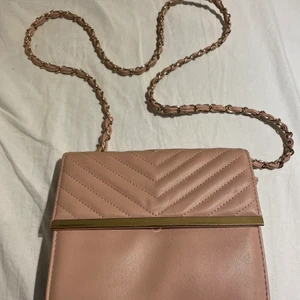 Handväska  - Säljer min rosa guldiga axelväska/ handväska, mycket fint skick dock så sitter knappen lite löst men funkar precis som vanligt ändå. Buda från 100kr. 