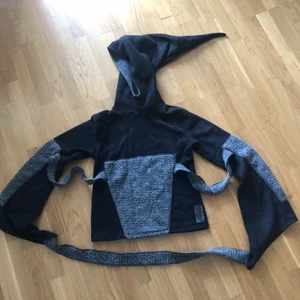 Nubia luva - Unik kofta/hoodie från Nubia. Detaljer med band, ,hög krage, utsvängda armar och spetsig luva. Grå och svart. Passar s-l. 