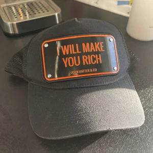 Svart John Hatter keps med citat ”I will make you rich” - En svart John Hatter keps med citatet ”I will make you rich” från filmen The Wolf Of Wallstreet (2013) Kepsen är ej använd mycket och säljer den då jag har många kepsar. Ursprungspris: 995kr