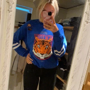 Sweatshirt - Blå sweatshirt med Tigertryck på och vita ränder på ärmarna. Lite slitningar/hål som tillhör tröjan på olika ställen. I storlek S. Knappt använd och säljs för 60kr+frakt 