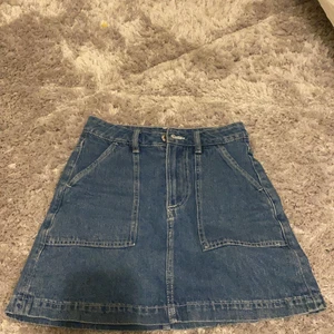 Jeans kjol - Säljer min fina jeans kjol från hm. De. Har stora fickor och en silvrig knapp. Den är gjort av jeans material. Den är mörkblå. GRATIS FRAKT!!