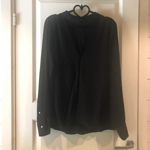 Blus med guldknappar - Blus med guldknappar i ärmslut och i nacken. Band vid halsen och djup v-ringning. 