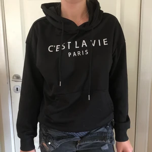 Hoodie - Svart hoodie med text ”c’est la vie paris” på framsidan. Vet tyvärr inte vart den kommer ifrån och det framkommer inte heller på lappen.