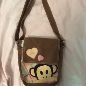 brun Frank Paul väska - Brun gullig frank paul väska med ett råsa rutigt mönster på och en apa 💕Fet finns en brun ficka med dragkedja och det finns också dragkedja till att stänga väskan❤️ Den är från second hand och har troligen används en del:) Den är brun på baksidan också och akselbandet är justerbart 🌸(det är lite svarta märken på apan som man ser och lite små trådar som knappt märks) 