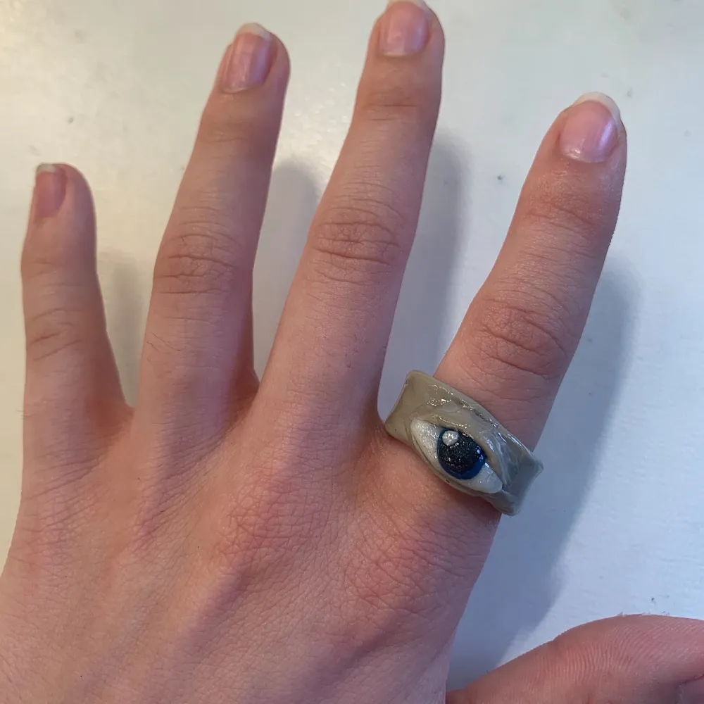En beige ring med ett blått öga, gjord i lera👁✨. Asusteet.