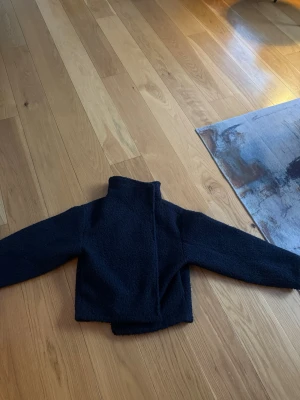 Mörkblå teddyjacka med hög krage - Mysig svart teddyjacka med hög krage och rak passform. Jackan är tillverkad i ett fluffigt teddy-material som håller dig varm och ger en trendig look. Perfekt för kyliga dagar när du vill vara både bekväm och snygg.