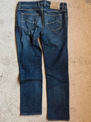 Mörkblå raka jeans från Jacob cohen - Säljer ett par mörkblå jeans från Jacob cohen med raka ben och klassiska kontrastsömmar. Jeansen har fem fickor och tydliga sömdetaljer på bakfickorna. Materialet är denim i bomull med en snygg tvättad look.