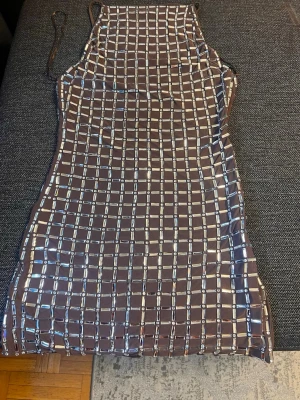 Brun kort klänning med paljetter - Supersnygg brun kort klänning med tunna axelband och ett rutigt mönster av silvriga paljetter. Klänningen har en figurnära passform och är perfekt för dig som vill sticka ut. Materialet känns mjukt och stretchigt, vilket gör den bekväm att bära hela kvällen.OBS! Ingen retur 🔊🔊🔊