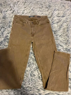 Bruna jeans från Dressmann - Snygga bruna jeans från Dressmann med klassisk femficksmodell och raka ben. Jeansen har bälteshällor, knappgylf och är tillverkade i ett mjukt bomullsmaterial med lite stretch för extra komfort. Perfekta för en avslappnad och stilren look.