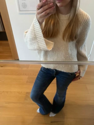 Vit ribbstickad tröja med slits - Säljer en krämvit ribbstickad tröja med rund hals och långa ärmar. Tröjan har en avslappnad passform och slitsar i sidorna för extra detalj. Perfekt till jeans eller kjol för en enkel och snygg look. 